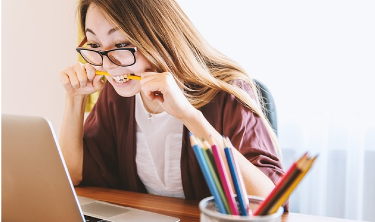 PCの前で鉛筆をかじりながら考え込む女性